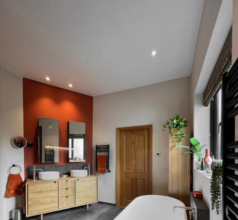 Photo of a bathroom installation in Wilmslow, Cheshire. shows a freestanding white resin bath, black wall mounted towel radiators, dark grey porcelain flor tiles and a oak vanity unit
